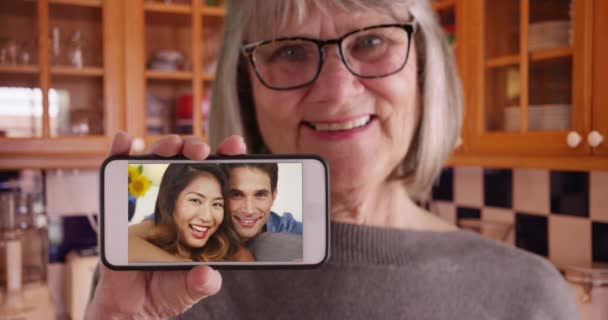 老太太一边拿着手机拍照 一边和儿子和女朋友聊天 白色老年女性手持电话 银幕上有快乐的白人男子和亚裔妇女 — 图库视频影像