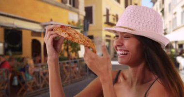 Roma, İtalya 'da sokakta pizza yiyen neşeli bir turist kadın. Yaz tatilinde İtalyan kültürünü ve mutfağını keşfeden modaya uygun genç bir bayana yakın durun. 4k
