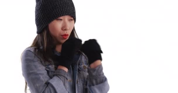 寒冷的千禧年女性试图保持温暖穿着便帽和手套在复制空间 年轻的亚洲女人用手套擦拭她的脸 在白色上取暖 — 图库视频影像