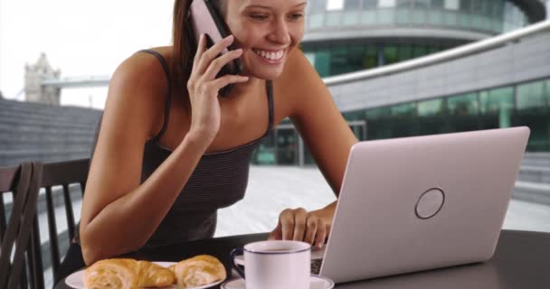 イギリスの観光客の女性は携帯電話で話し ラップトップで働いています 陽気な若い女性が屋外でコーヒーを飲み 携帯電話でチャット — ストック動画