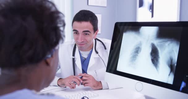 成人男性医師の肖像は 彼女の研究室の結果を中年アフリカの女性に説明する 患者にコンピュータ上の彼女の肺のX線を示す男性医師の閉鎖 — ストック動画