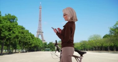 Paris 'teki Eyfel Kulesi' nin önünde motosikletli bir kadın cep telefonuyla mesaj atıyor. Fransa 'da tatilde bisiklet durakları olan yetişkin bir Kafkasyalı turist akıllı telefondan mesaj gönderiyor. 4k