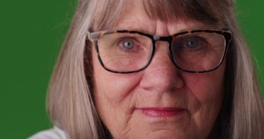 Kapalı alanda yeşil ekran stüdyosunda reçeteli gözlüklü son sınıf beyaz kadının yakın çekimi. Yeşil ekranın önünde yaşlı ve kasvetli bir kadının gözlük taktığı görüntüler. 4k