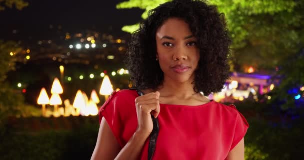 拍摄迷人的年轻黑人女子的肖像 可以看到夜晚的城市灯光 迷人的非洲裔美国人在温暖的夜晚手握钱包 — 图库视频影像