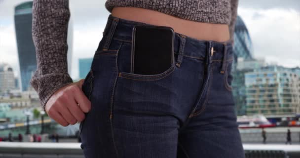 年轻女士腰部的特写 口袋里有电话 背景是城市景观 在大都市里 一个带着手机的女孩站在中间的特写镜头 — 图库视频影像