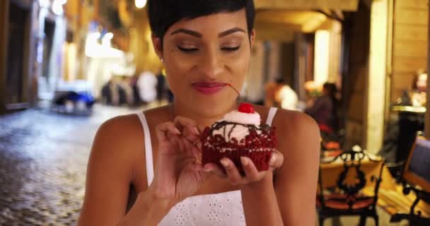 黒の女性は派手な赤いベルベットのカップケーキの乱雑な一口を取ります アフリカ系アメリカ人女性は喜んで彼女の食事療法をカンニングする — ストック動画