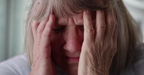 有压力的老年妇女在家中面对痛苦的特写镜头 老年妇女偏头痛的特写镜头 脸上带着痛苦的表情擦着头 — 图库视频影像