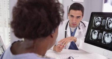 Siyahi bir kadın, kafatası taramalarına doktorların bilgisayarından bakıyor. Genç Latin doktorların portresi hastaların beyin taramalarındaki anormalliği ve baş ağrısına neyin sebep olabileceğini açıklıyor.