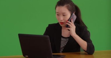 Yeşil ekranda akıllı telefon ve dizüstü bilgisayar kullanan profesyonel bir iş kadını. Genç Asyalı sekreter kadın iş yapmak için teknolojiyi kullanıyor. 4k