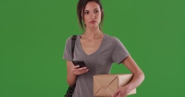 Kadın, paketi yeşil ekranda tutarken telefon üzerinden nakliye uygulamasını kontrol ediyor. Millennial paketleri izlemek için akıllı telefon kullanıyor