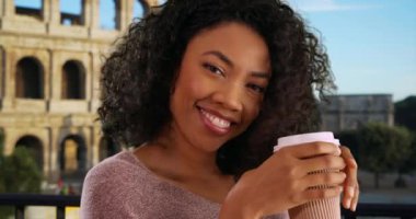 Siyahi kadın turistin Roma 'da tatilde Colosseum' un dışında kahve içişini. İtalya 'da tatilde Afrika kökenli Amerikan milenyumu bardak kâğıdı tutuyor. 4k