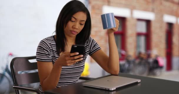 快乐的黑人妇女用她的笔记本电脑和咖啡手机 兴高采烈的女商人在下班后 用智能手机给朋友发短信大笑 — 图库视频影像