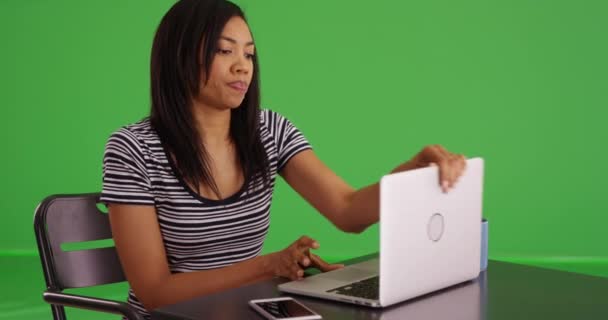 黒の女性はノートパソコンで作業を終了し 蓋を閉じてから 画面上のカメラを見ています アフリカ系アメリカ人の女性がノートパソコンで緑の画面で休憩している — ストック動画