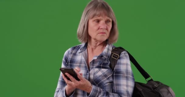 緑色のクロマキーの背景に隔離されたナビゲーションのためのスマートフォンデバイスを使用して高齢女性を混乱させました 緑の複合体上の携帯電話を保持高齢者の女性を失った — ストック動画
