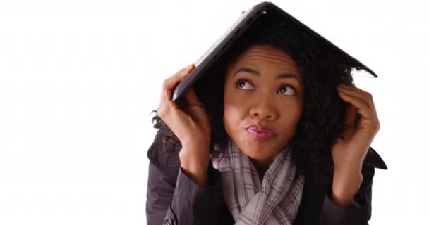 接近漂亮的黑色女性 头顶着笔记本电脑 在白色背景下保护自己不受天气的影响 忧心忡忡的非洲裔美国女人用电脑在工作室里用版权保护自己 — 图库视频影像