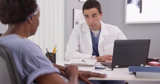 Pacientul African Vârstă Întâlnește Tânăr Medic Latino Biroul Său Explicând — Videoclip de stoc