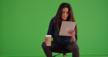 Latin iş kadınının portresi dokunmatik ekranı kullanıyor ve yeşil ekranda kahve içiyor. Anahtar ya da birleşik olmak üzere yeşil ekranda.