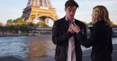 Paris 'te akıllı telefon kullanan çekici bir milenyum çifti. Bir adam ve bir kadın cep telefonu kullanarak Seine nehrinin kenarında dururlar. 4k