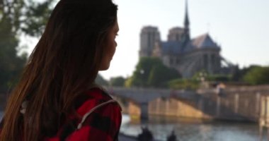 Flanel ceketli hippi kız Seine Nehri 'ni izliyor. Paris 'i gezen Millennial kadın Notre Dame Katedrali' nin yakınındaki Seine 'in yanında duruyor. 4k