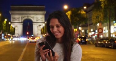 Güzel bir kadın, Arc de Triomphe 'nin arkasında olduğu şehir caddesinde telefonunun selfie' sini çeker. Turist kadın, arkadaşlarıyla paylaşmak için gece Paris 'in simgesi yakınlarında fotoğraf çekiyor. 4k