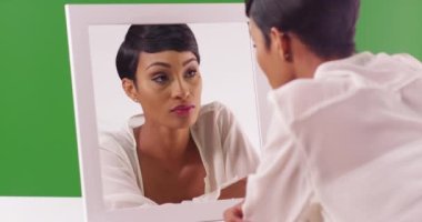 20 'li yaşlarındaki muhteşem siyah kadın yeşil ekrandaki aynadaki yansımaya bakıyor. Anahtar ya da birleşik olmak üzere yeşil ekranda.