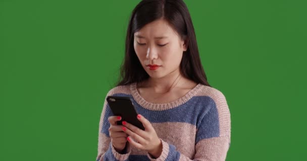 用智能手机在绿色屏幕上发送短信的年轻中国学生的特写 亚洲女人在绿色铬基复合材料上与手机即时通讯的肖像 — 图库视频影像