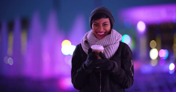 美丽的黑色女性画像 裹着围巾 晚上站在喷泉边笑着 在寒冷的秋夜 20多岁的可爱女人在户外端着咖啡杯 — 图库视频影像