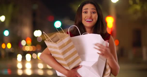一个年轻的拉美女人抱着购物袋 对着相机笑的画像 快乐的购物狂挣扎着把她的购买在城市街道上的夜晚 — 图库视频影像