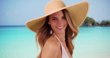 Karayipler 'de plajda beyaz şapkayla poz veren beyaz kadın portresi. Virgin Adaları 'ndaki okyanus kenarında çekici kadın modellik modasına yakın çekim. 4k