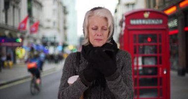 Londra 'da tatilde olan yaşlı bir kadın cep telefonu ve bir fincan kahveyle gezintiye çıkmayı bekliyor. Emekli emekli, akıllı telefon haritası uygulaması kullanarak İngiltere 'ye tatile gidiyor. Kışın giyinmiş bir kadın. 4k