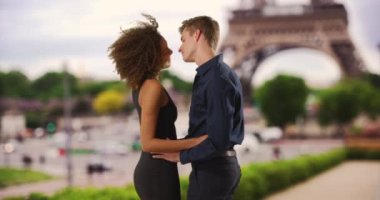 Mutlu çift Eyfel Kulesi yakınlarında birbirlerinin gözlerinin içine bakıyor. Beyaz erkek ve Afrikalı kadın balaylarında Paris 'te. 4k