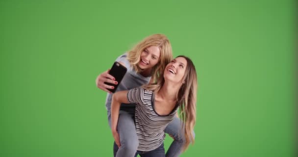 两个漂亮的女孩玩仰卧起坐和拿着智能手机相机在绿屏上自拍 女朋友搭便车回来 在绿色荧幕上自拍 — 图库视频影像