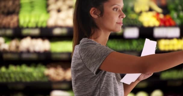 棚の上の製品を通して見てフィット感と健康的な女性の顧客の閉鎖 ショッピングリストで最高の製品を選択している若い女性スーパーマーケット — ストック動画