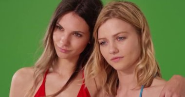 Yeşil ekranda duran kasvetli yüzlü iki beyaz kızın portresini yakından çek. Yeşil ekran duvarının önünde üzgün görünen güzel genç kadınların dar bir görüntüsü. 4k