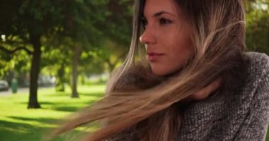 Park ortamında rüzgarda esen uzun kahverengi saçlı güzel bir kadın. Düşünceli ve ciddi bir genç bayan parkın dışına bakıyor. 4k
