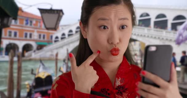 ヴェネツィアイタリアのリアルト橋の前で自撮りや伝統的な中国のファッションを身に着けている幸せな千年紀の女性の笑顔を閉じます スマホでアジアの女性を笑顔にして自撮り — ストック動画