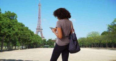 Siyahi kadın turistin Eyfel Kulesi 'nin önünde mesaj gönderdiğini gördüm. Akıllı telefon kullanarak Paris 'te tatilde olan Afrikalı Amerikalı bir kız. 4k