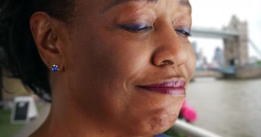 Yaşlı siyahi kadının Thames nehrine bakıp gülüşünü ve gülüşünü yakından çek. Kule Köprüsü 'nün yanında neşeli Afrikalı Amerikalı kadın turist duruyor. 4k