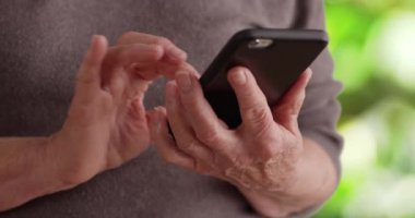 Yetişkin bir kadının mesajları okumak için akıllı telefon kullanması. Doğa ortamında cep telefonuyla mesajlaşan yaşlı birinin eli sıkıdır. 4k