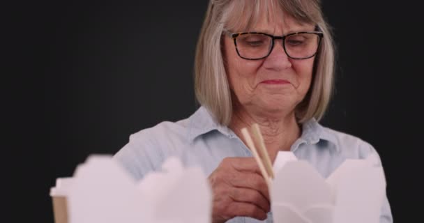 灰色の背景に彼女の幸運クッキーを披露幸せな高齢者の女性 しっかりとした灰色の背景に幸運を読んで楽しい先輩女性の肖像画 — ストック動画