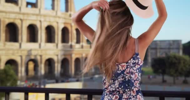 若い女性がフェドーラを離陸し イタリアのローマで髪を下ろすの背面図 20代の女性は ローマのコロシアムによって帽子を取り出し 髪を通して手を走らせています — ストック動画