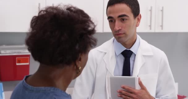 用便携式平板电脑对年轻的拉蒂诺医生进行近距离观察 讨论病人的病史 有魅力的年轻医生与非洲老年妇女谈论健康问题 — 图库视频影像