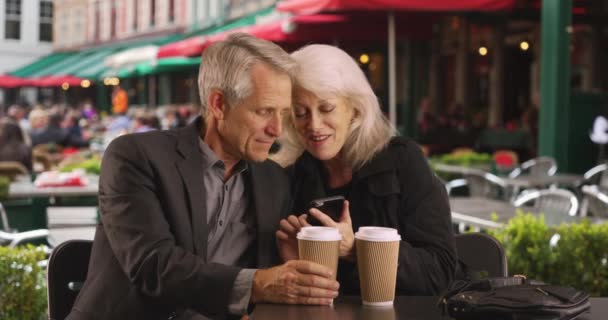 スマホで可愛い写真を見ている熟女妻と夫 携帯電話を使用してブルージュの観光カップル — ストック動画