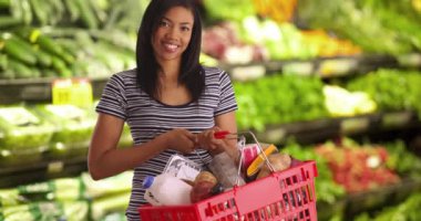 Süpermarkette elinde market sepeti tutan güzel Afro-Amerikan kadın portresi. Markette kameraya gülümseyen neşeli bir müşteri. 4k