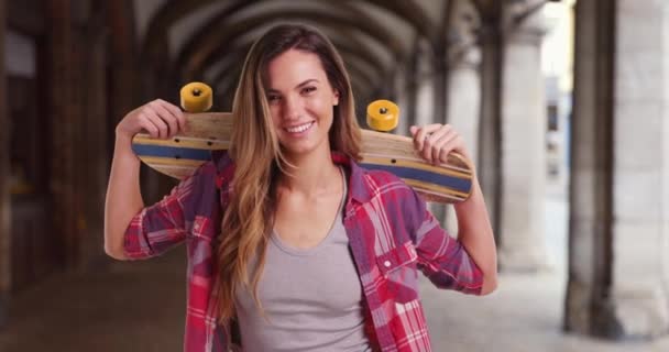幸せ白人女性は彼女の肩の上にスケートボードを保持 彼女のスケートボードのカメラで笑顔でクールなヒップスター女性 — ストック動画