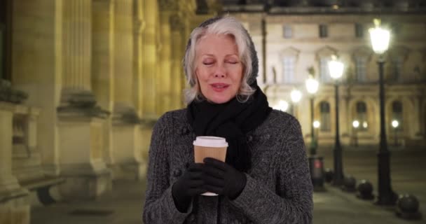 Szczęśliwa Seniorka Drżąca Zimną Noc Trzymając Filiżankę Kawy Pod Latarnią — Wideo stockowe