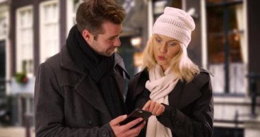 Mutlu milenyum çiftleri akıllı telefonlarıyla dışarıda konuşuyorlar. Modern bir çift yemek yiyecek bir yer bulmak için akıllı telefon kullanıyor. 4k