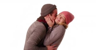 Kışın giyinmiş genç bir çift beyaz arka planda kucaklaşıyorlar ve sevecen davranıyorlar. Gülümseyen kız ve erkek arkadaş, stüdyoda birbirlerinin gözlerinin içine bakıp öpüşüyorlar. 4k