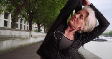 Yetişkin koşucu şehirde koşmak için ısınıyor. Akıllı bacaklı sağlıklı bir atletik kadın müzik dinlerken koşuya çıkar. 4k