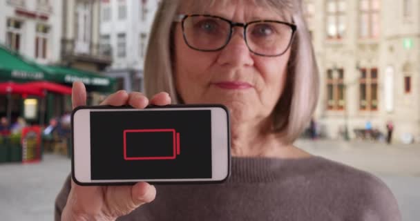 Sênior Feminino Segurando Telefone Até Câmera Com Indicador Bateria Fraca — Vídeo de Stock